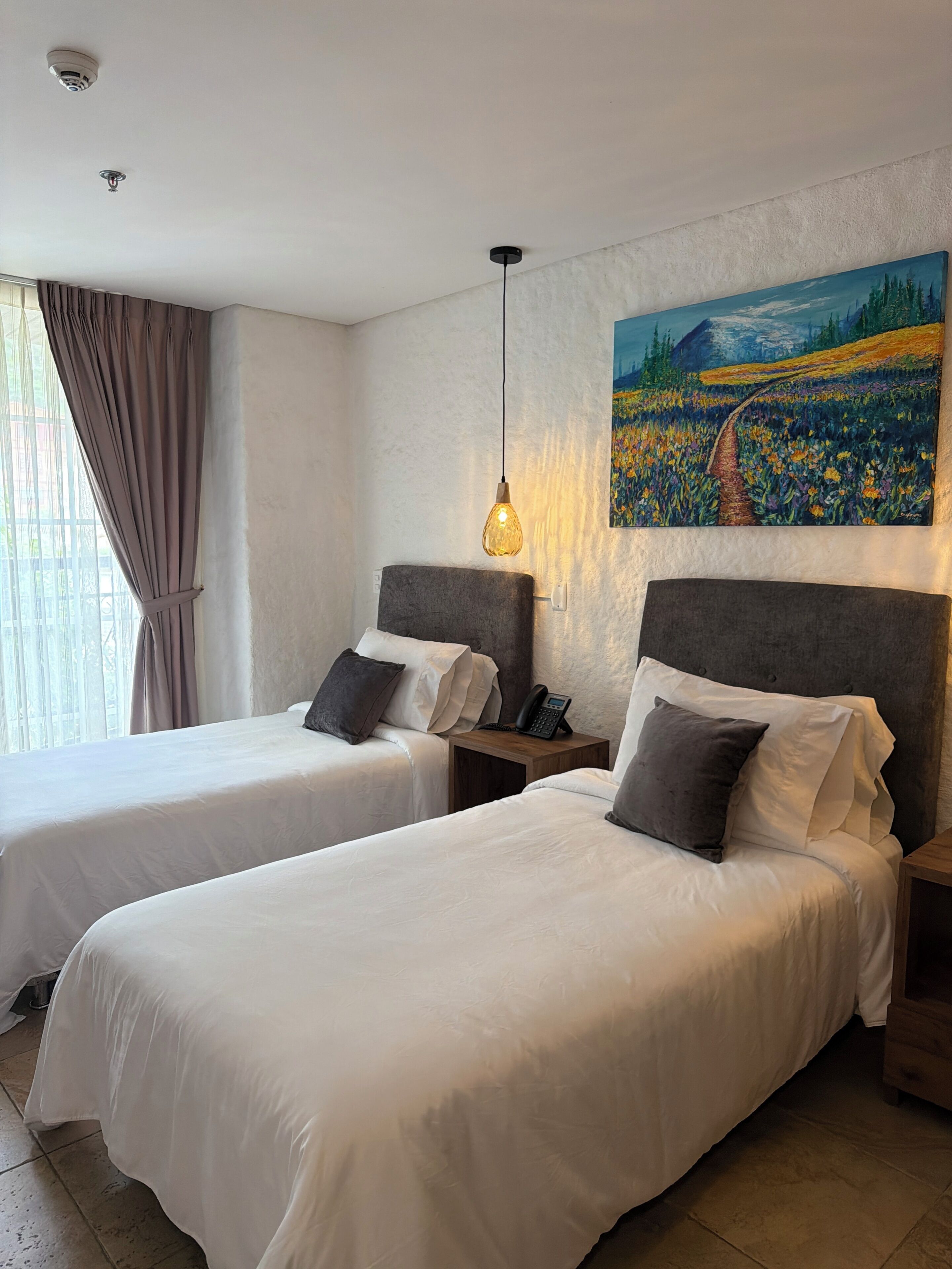 Habitación de hotel con dos camas, un cuadro en la pared, un teléfono en la mesita de noche y una lámpara colgante.