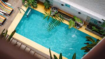 Una piscina con borde de azulejos, rodeada de plantas y una silla de descanso.
