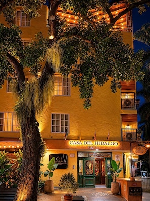 A hotel with a sign reading 'CASA DEL HIDALGO HOTEL,' a large tree in front, and a well-lit entrance. - Hotel Casa del Hidalgo Centenario - Business & Leisure (Cali)