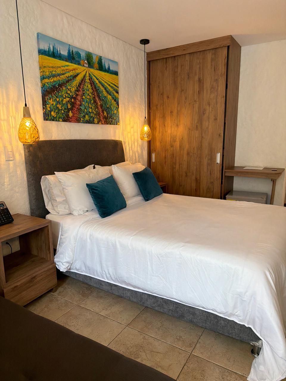 A bedroom with a bed, wooden headboard, bedside tables, a painting on the wall, and a wardrobe.