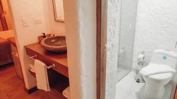 A bathroom with a wooden vanity, a round sink, a toilet, and a glass shower enclosure.