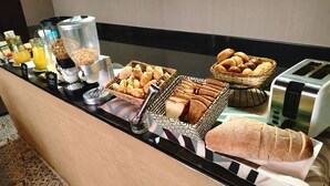 Un bufé de desayuno con diferentes alimentos, una tostadora y un panecillo.