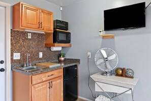 Cocina compacta con armarios de madera, microondas, lavavajillas, pileta, ventilador y un televisor de pantalla plana montado en la pared.