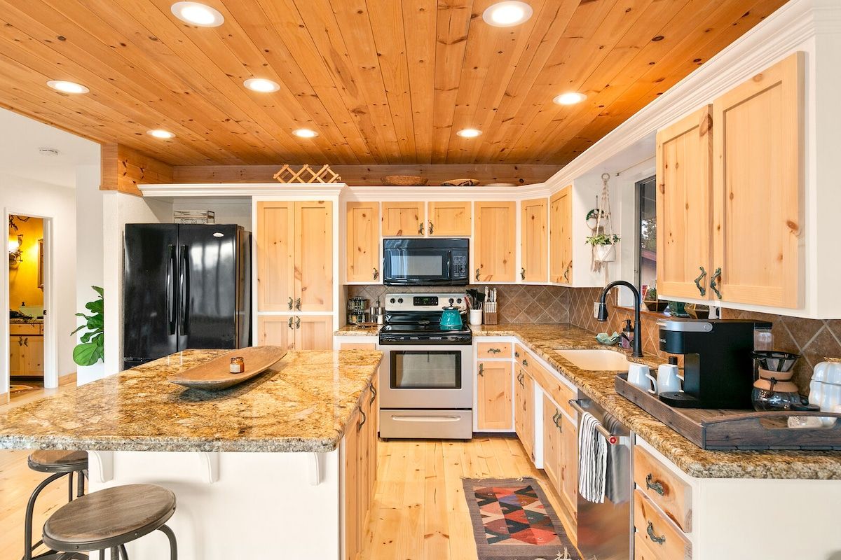 A kitchen with wooden cabinets, granite countertops, a black refrigerator, a microwave, an oven, and a coffee maker.