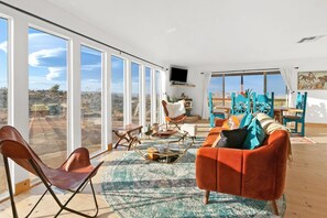Un salón amplio con un gran ventanal, un sofá, una mesa de centro y un televisor montado en la pared.