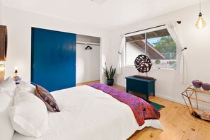 A bedroom with a bed, a wardrobe, a window with curtains, a plant, and a decorative item on a side table. - High View Haven - 5min to Park, Hot Tub, Fire Pit, BBQ (Joshua Tree)