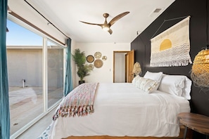 A bedroom with a bed, a ceiling fan, a large window, and a wall with decorative items.