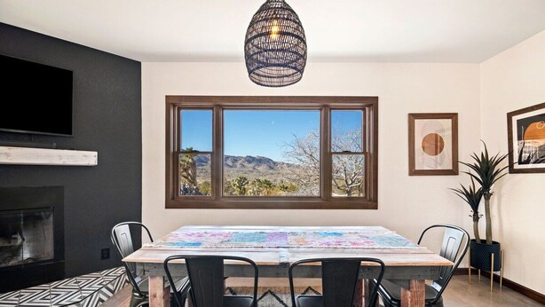 A dining area with a table, chairs, a fireplace, a large window with a view, and a hanging light fixture.