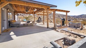 A covered patio area with outdoor seating, a hot tub, and a view of the surrounding desert landscape.