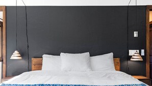 A bed with white bedding and a blue patterned throw, against a dark wall with two hanging lamps.