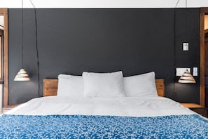 A bed with white bedding and a blue patterned throw, against a dark wall with two hanging lamps. - Dreamspace - Hot Tub, Fire Pit & MInutes to Park! (Joshua Tree)
