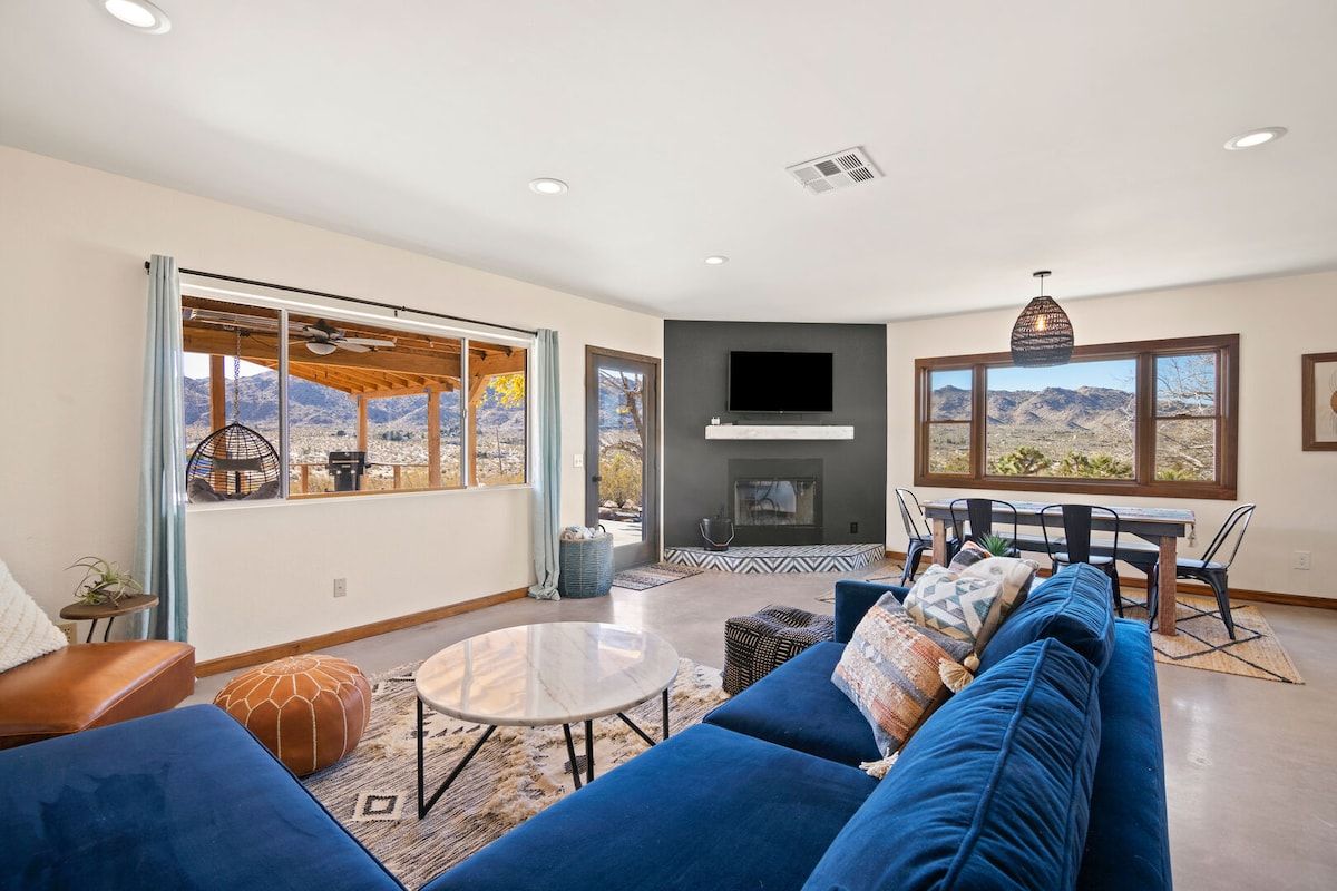 A modern living room with a fireplace, large windows, and a view of mountains.