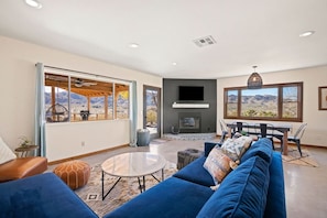 A modern living room with a fireplace, large windows, and a view of mountains. - Dreamspace - Hot Tub, Fire Pit & MInutes to Park! (Joshua Tree)