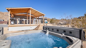 A hot tub with a wooden deck and a covered area, surrounded by a desert landscape. - Dreamspace - Hot Tub, Fire Pit, 5 Min to Park! (Joshua Tree)