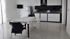 A modern kitchen with white cabinets, a dining table with chairs, and a flat-screen TV mounted on the wall. - Apartamento Amueblado en Santo Domingo (Santo Domingo)