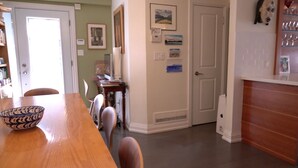 Un'area pranzo con un tavolo e sedie in legno, una cucina con frigorifero e pensili, e una porta che dà su un'altra stanza.