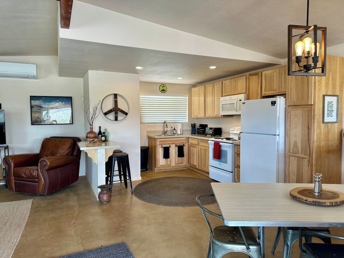 Une cuisine moderne avec des meubles en bois, un coin repas comprenant une table et des chaises, un fauteuil en cuir et un luminaire suspendu.