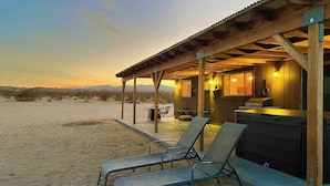 Eine Strandhütte mit einer überdachten Terrasse, Liegestühlen und einem Whirlpool.