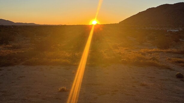 Paisaje desértico con atardecer, cielo despejado y colinas distantes.