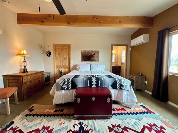 A bedroom with a bed, a wooden bench, a dresser, a suitcase, and a wall-mounted air conditioner.