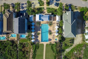 Vista aérea de un complejo turístico con varias edificaciones, una piscina central y palmeras a su alrededor.