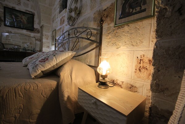 A bedroom with a wooden nightstand, a bed with floral bedding, and a wall with a stone texture.
