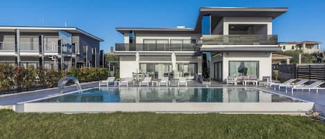A modern residential building with a swimming pool, lounge chairs, and a well-maintained lawn.