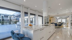 Eine moderne Küche mit einer Marmor-Kochinsel, großen Fenstern und einem Essbereich mit einer Chandelier.