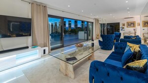 Ein modernes Wohnzimmer mit einem Glastisch, blauen Sofas und einem großen Fenster mit Blick auf die Stadt.