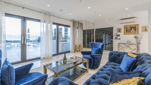 Ein modernes Wohnzimmer mit einem Glastisch, blauen Sofas und Meerblick durch große Fenster.