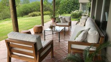 An outdoor patio with wooden furniture, including a sofa and chairs, a small table, and a potted plant.
