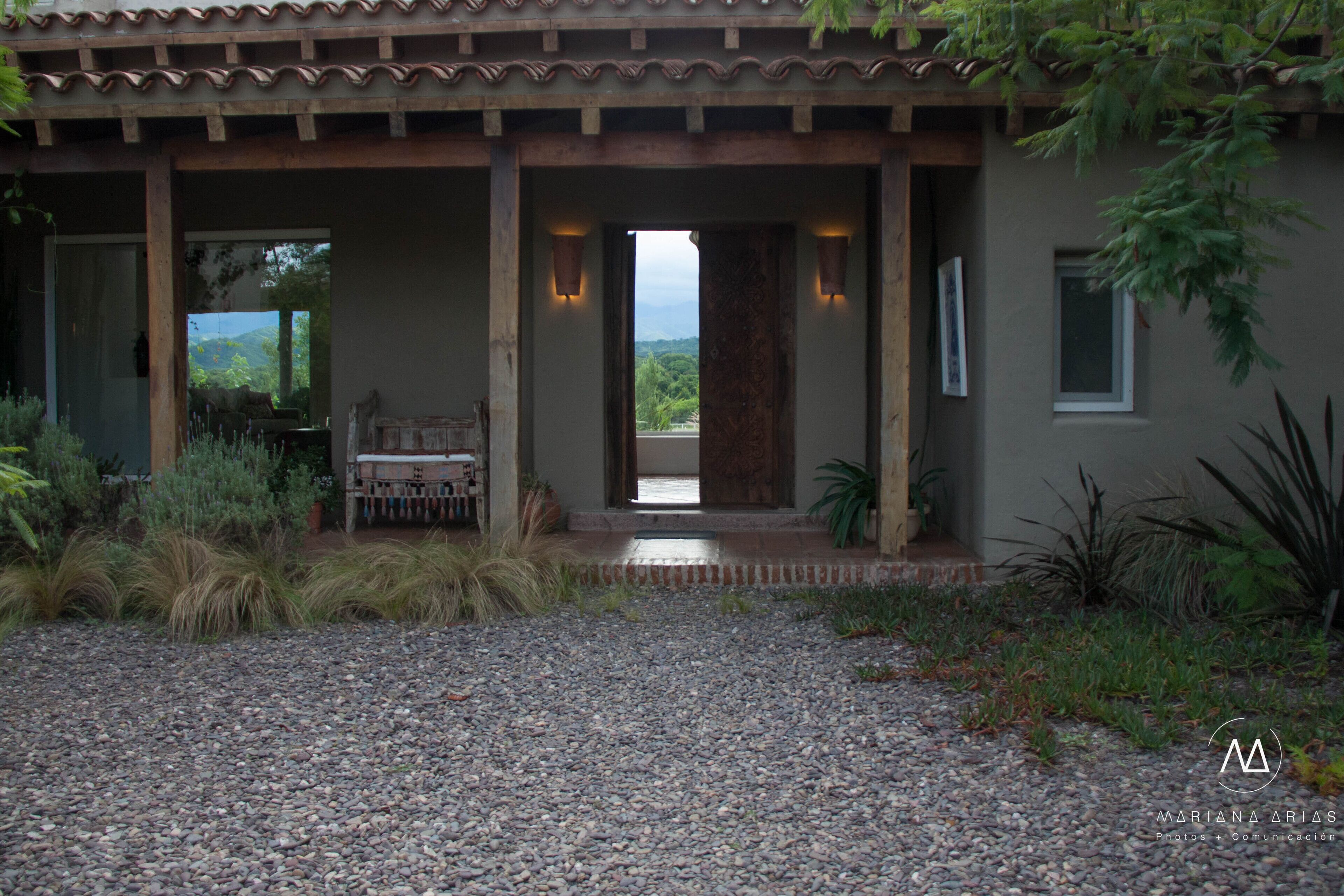 A building with a covered entrance, a gravel driveway, and a view of greenery in the background.