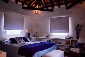 A bedroom with a bed, two windows with blinds, a nightstand, a chair, and a bookshelf. - Espectacular Casa Con Increíble Paisaje (Salta)