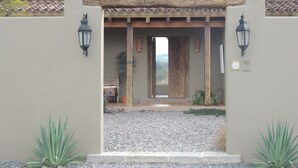 A building entrance with a wooden door, two wall-mounted lanterns, and a gravel pathway.