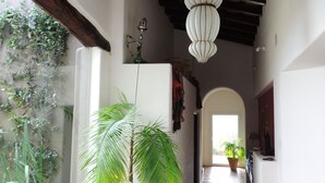 A hallway with a tiled floor, a large potted plant, a hanging light fixture, and a view of the outdoors.