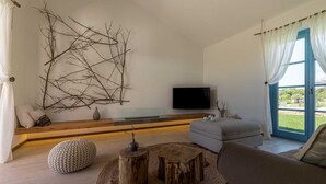 A modern living room with a large branch wall art, a flat-screen TV, a grey sofa, and a wooden coffee table.
