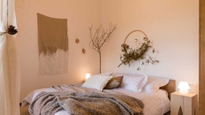 A bedroom with a bed, a bedside table, a wall-mounted plant, and a painting.