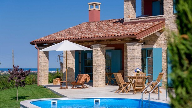 A two-story stone house with a swimming pool, outdoor furniture, and a view of the sea.