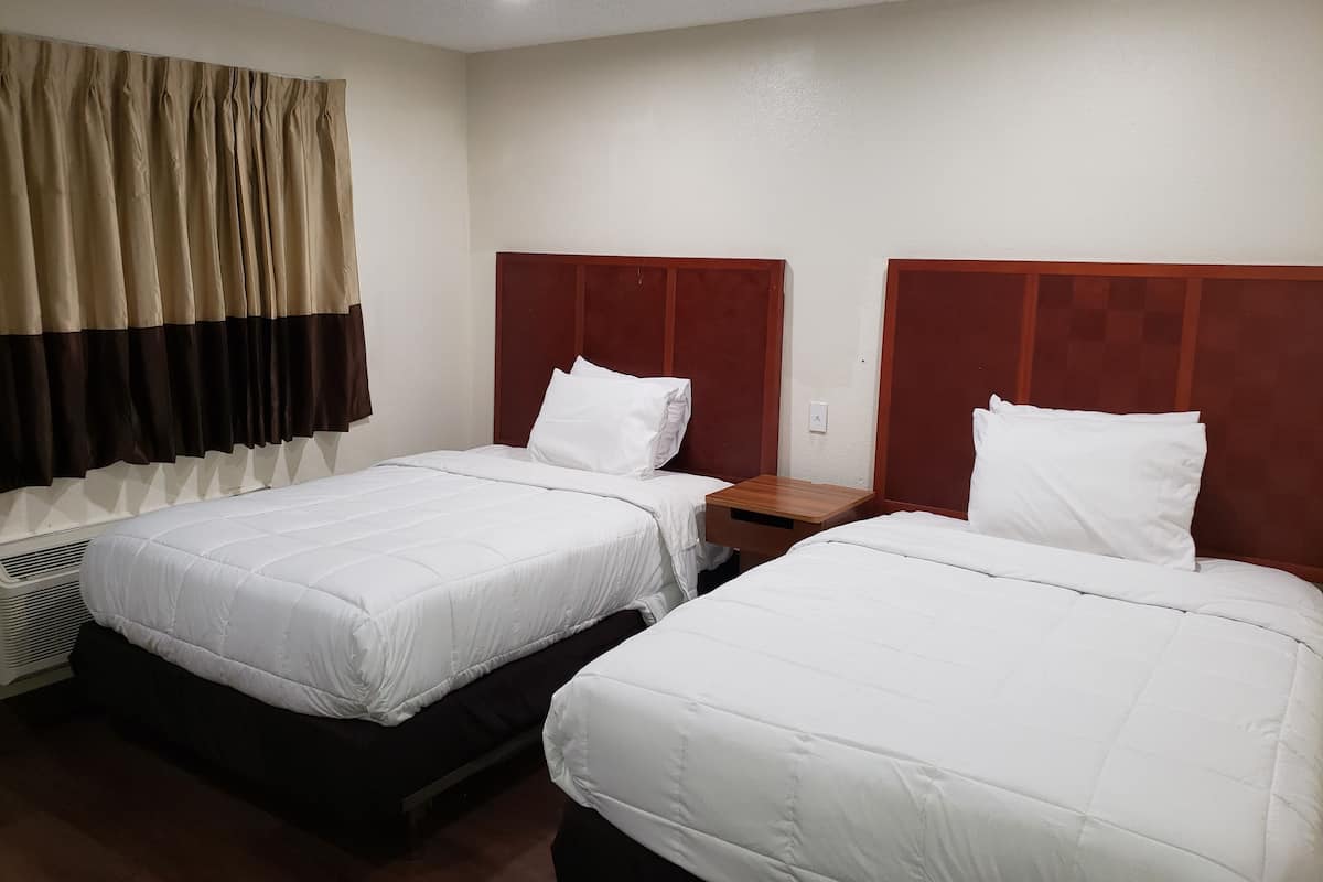 A hotel room with two beds, each with white bedding and wooden headboards.