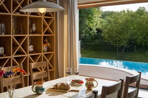 A dining area with a table set for two, a wooden bookshelf, and a view of a swimming pool. - Luxury Villa Retreat with Infinity Pool (Labin)