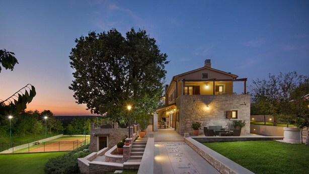 A two-story house with a stone facade, a tennis court, and a well-lit outdoor area. - Luxury Villa Retreat with Infinity Pool (Labin)