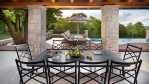 An outdoor patio with a dining table, chairs, and a pool in the background. - Luxury Villa Retreat with Infinity Pool (Labin)