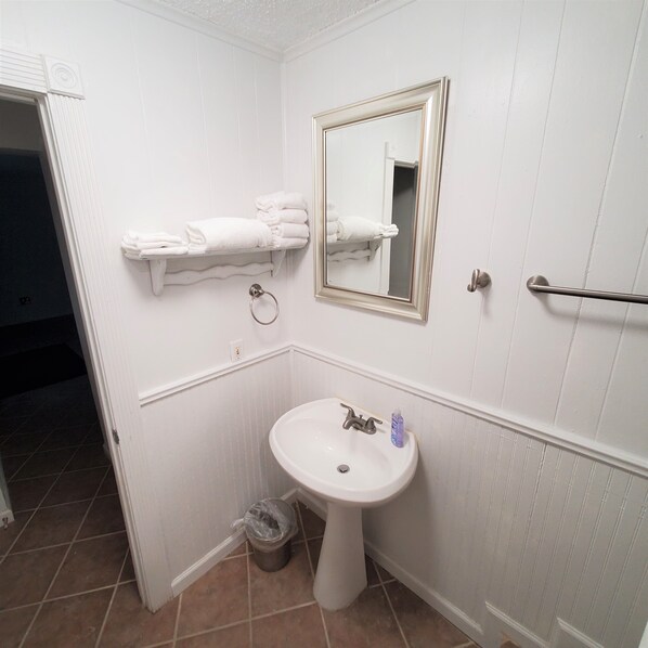 A bathroom with a pedestal sink, a mirror, a towel rack, and a trash can.