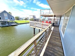 A wooden deck with a view of a body of water, a covered seating area, and a building in the background.