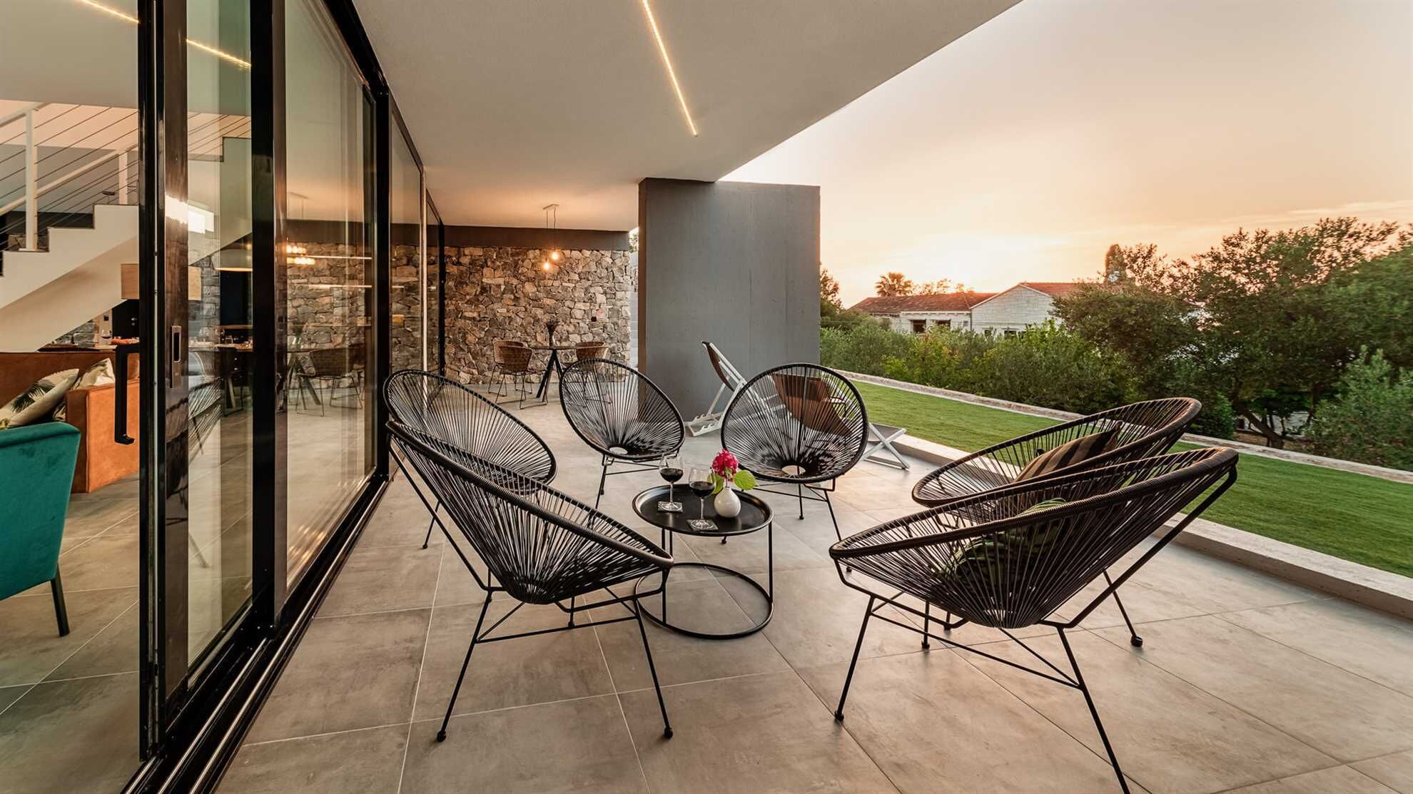 A modern outdoor patio with wicker chairs, a round table, and a stone wall.