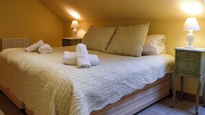 Ein ordentlich gemachtes Bett mit einer Steudecke, zwei Kissen und aufgerollten Handtüchern. Es gibt zwei Nachttische mit Lampen.