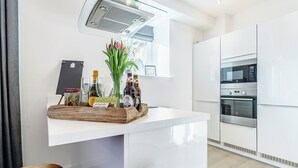 A modern kitchen with white cabinetry, a built-in oven, and a glass-top island with a tray of bottles and a vase of flowers. - 2 bedroom accommodation in Alnwick (Alnwick)