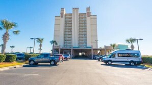 A multi-story hotel with a central entrance, parking lot, and palm trees. - Royal Palms 1002 by Liquid Life (Gulf Shores)