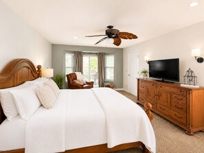 Une chambre à coucher avec un grand lit, une commode en bois, un téléviseur et un ventilateur de plafond.