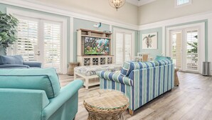 A spacious living room with a large television, comfortable seating, and a decorative ceiling light. - Beach Haven Private Heated Dip Pool! (Palm Coast)